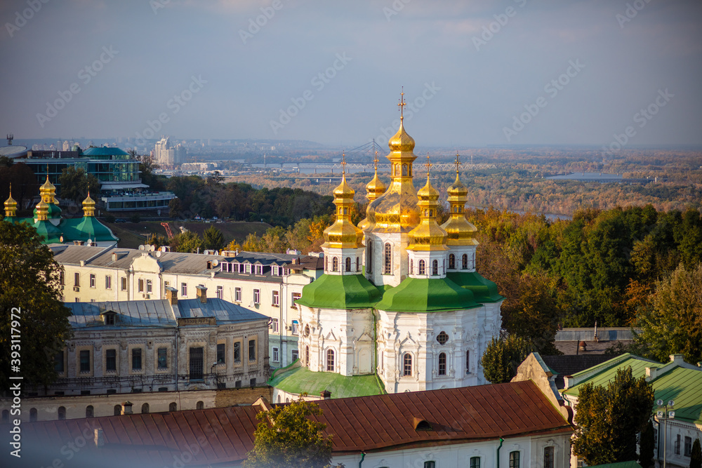 Beautiful yellow and gold domes of the Orthodox Church against the background of the blue sky and the city. Domes of the Assumption Cathedral of the Kiev-Pechersk Lavra.