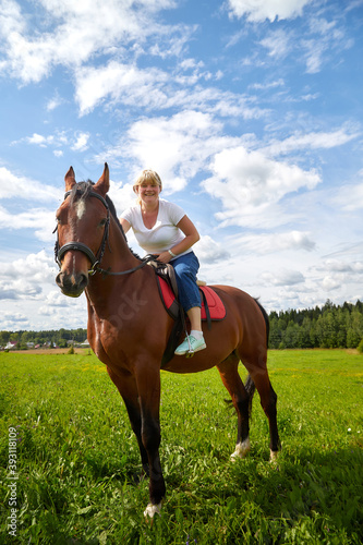 Girl riding on a horse on a green field and a blue sky with white clouds on the background