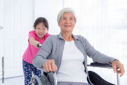 Fototapeta Happy old senior woman and young girl ride in wheelchair at nursing home