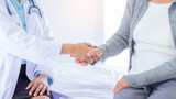 Close up doctor shakes hands with a woman patient at hospital bed.