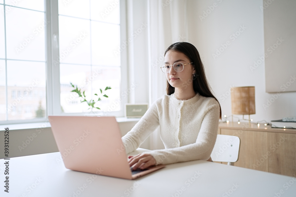 Cute teenager girl sitting at table and doing homework. Education concept, distance learning, self-education, video conference class with tutor Cute teenager girl sitting at table and doing homework. Education concept, distance learning, self-education, video conference class with tutor