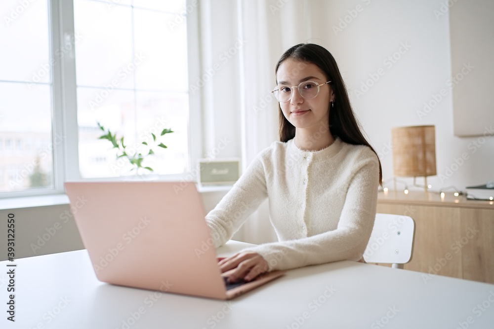 Cute teenager girl sitting at table and doing homework. Education concept, distance learning, self-education, video conference class with tutor Cute teenager girl sitting at table and doing homework. Education concept, distance learning, self-education, video conference class with tutor