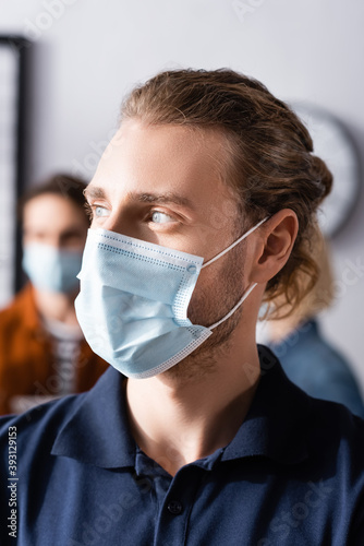 Manager in medical mask looking away in office on blurred background
