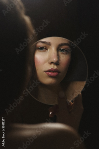 Young female holding mirror in her hand and looking at her reflection.