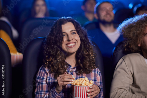 Young laughing girl eating popcorn in movie theater.