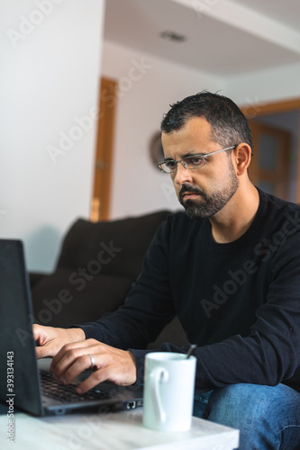 Man working from home on the couch with his laptop and a cup of coffee