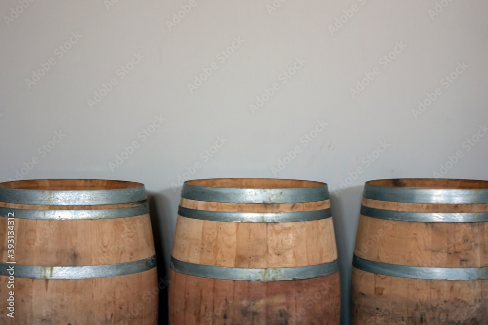 Fototapeta premium Three oak barrels stand against the wall. Wooden barrels are tied with steel hoops. Metal and natural wood of wine barrels