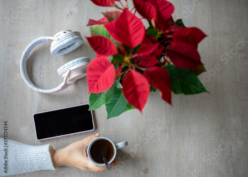 Top view of a table with a poinsettia, wireless headphones, mobile phone and a hand grabbing a cup of coffee