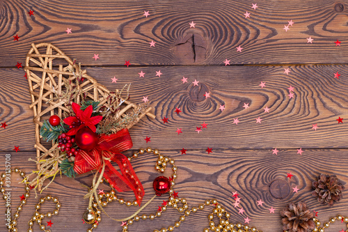 Golden bell from rattan with pine cones, Christmas toys, shiny beads and small red shiny stars on a wooden table. Top view, copy space photo