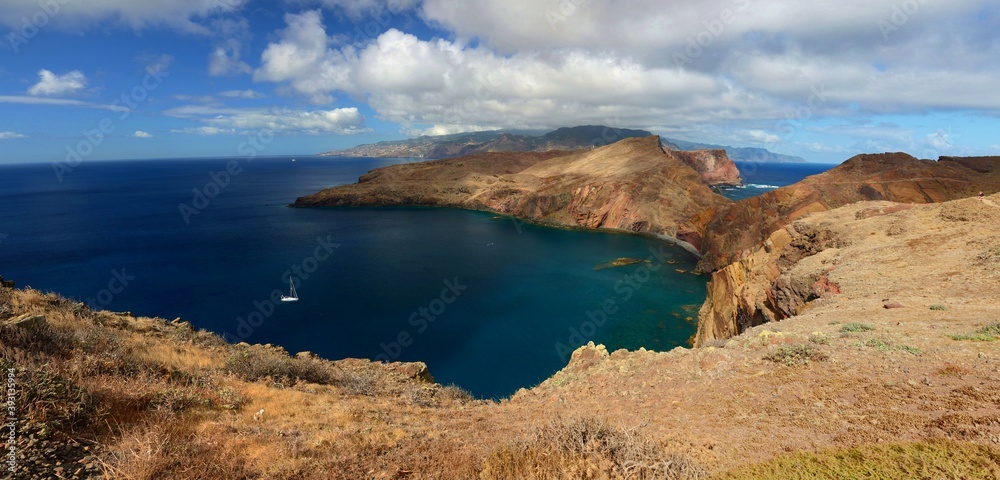 Atlantic Ocean in Madeira, Portugal. View of the ocean from the peninsula of St. Lawrence (São Lourenço). Sailboat in the middle, rocky cliffs, hiking trail, arid landscape.