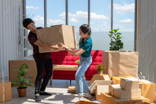 Young Asian couple moving house and carrying box in living room. Surround with many boxes. Lover develop relationship by living together. Home design and interior concept.