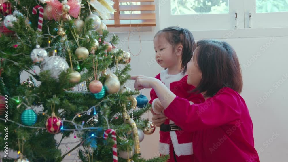 Happy Asian mother and toddler girl helping to decorate Christmas tree, festive season, season greeting, family activity quality time, mother daughter relationship Happy Asian mother and toddler girl helping to decorate Christmas tree, festive season, season greeting, family activity quality time, mother daughter relationship