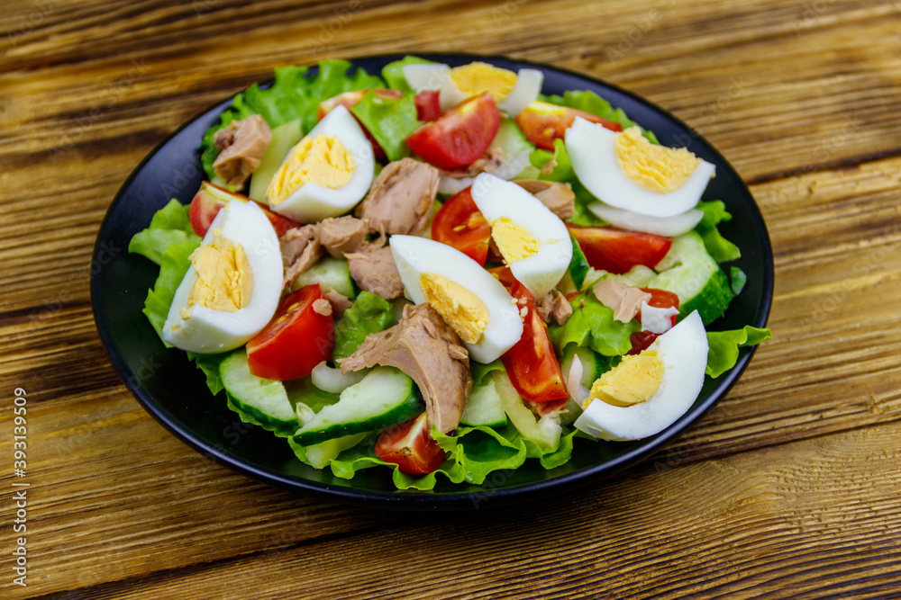 Tasty tuna salad with eggs, lettuce and fresh vegetables on wooden table