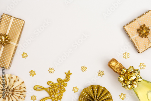 Festive background with gold decoration , gift boxes with bottle of sparkling wine, shiny golden serpentine confetti and paper christmas tree decorations, glittering snowflakes and christmas tree