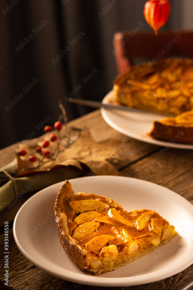 Apple pie with caramel on a wooden background, autumn bouquet in a vase, portion of pie in a plate close-up