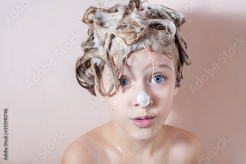 a little blonde girl washes her hair in the shower with foam on her hair and nose. playing in the bathroom with foam