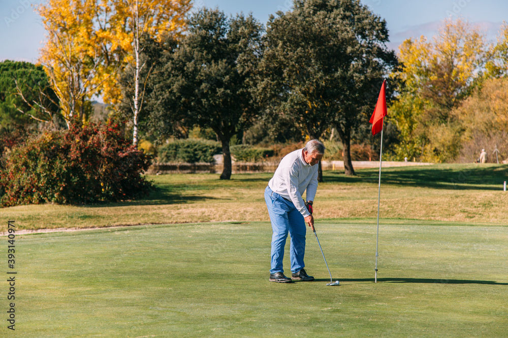 Obraz premium Senior golfer at putting green hitting ball into a hole