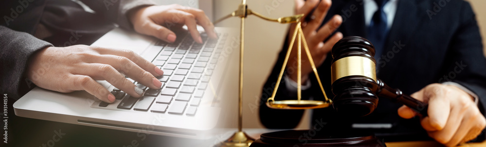 Justice and law concept.Male judge in a courtroom with the gavel, working with, computer and docking keyboard, eyeglasses, on table in morning light Justice and law concept.Male judge in a courtroom with the gavel, working with, computer and docking keyboard, eyeglasses, on table in morning light