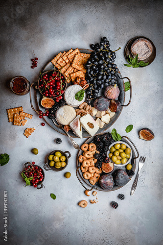 assortment of cheese, grape, berries, olives, figs and crackers on metal trays, party appetizer concept, top view