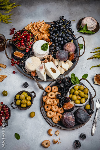 assortment of cheese, grape, berries, olives, figs and crackers on metal trays, party appetizer concept, top view