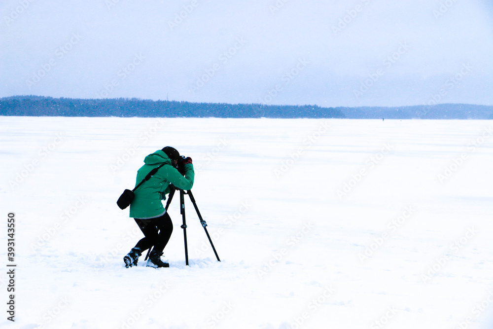 A WOMAN PHOTOGRAPHER WITH A GREEN JACKET TAKING PICTURES IN BEAUTIFUL LAPLAND, FINLAND. COLD AND SNOW CONCEPT.