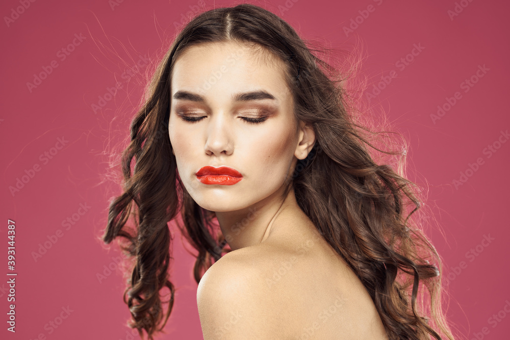 Fototapeta premium Beautiful brunette woman with makeup on her face on a pink background naked shoulders