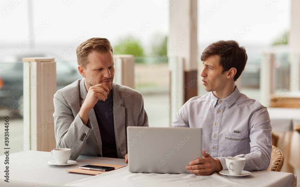 Two businessmen sitting at table at outdoor cafe, discussing business presentation on laptop screen and cooperation possibilities Two businessmen sitting at table at outdoor cafe, discussing business presentation on laptop screen and cooperation possibilities