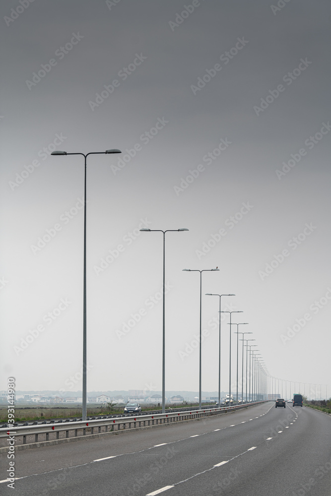 Repetitive street lights over a highway with a neutral grey background