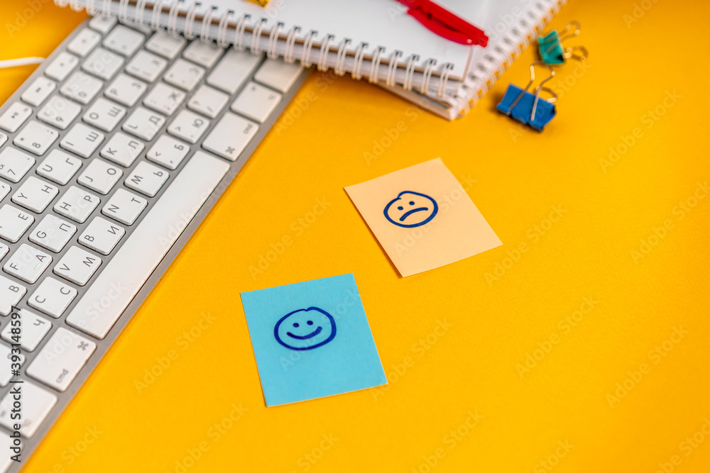 Sad and happy stickers on your desktop next to your keyboard and office supplies. The concept of emotionality of the person at work life concept Sad and happy stickers on your desktop next to your keyboard and office supplies. The concept of emotionality of the person at work life concept