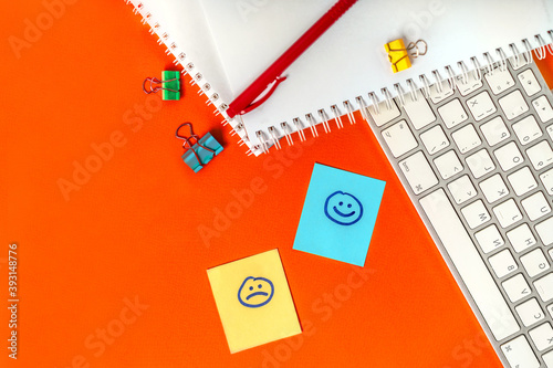 Sad and happy stickers on your desktop next to your keyboard and office supplies. The concept of emotionality of the person at work life concept
