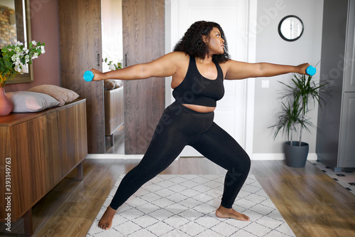 Fototapeta Naklejka Na Ścianę i Meble -  attractive afro american black female engaged in fitness at home, overweight woman is stretching and doing various sport exercises