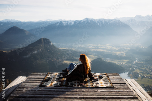 Back view of unrecognizable female tourist sitting at viewpoint in mountains and observing amazing scenery in morning