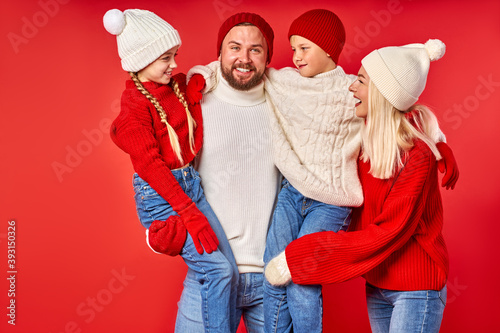 portrait of family having fun in winter clothes isolated over red studio background, young parents and children enjoy winter time, christmas photo