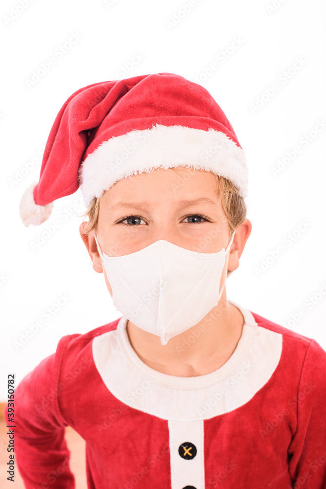 A child like Santa Claus, isolated on white background, wears a mask on his face to protect himself from viruses at Christmas. A child like Santa Claus, isolated on white background, wears a mask on his face to protect himself from viruses at Christmas.