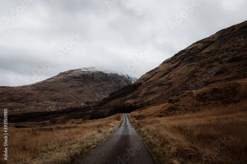 Road in between valley and amazing view of rocky mountain top with snow in fall in Scottish Highlands photo