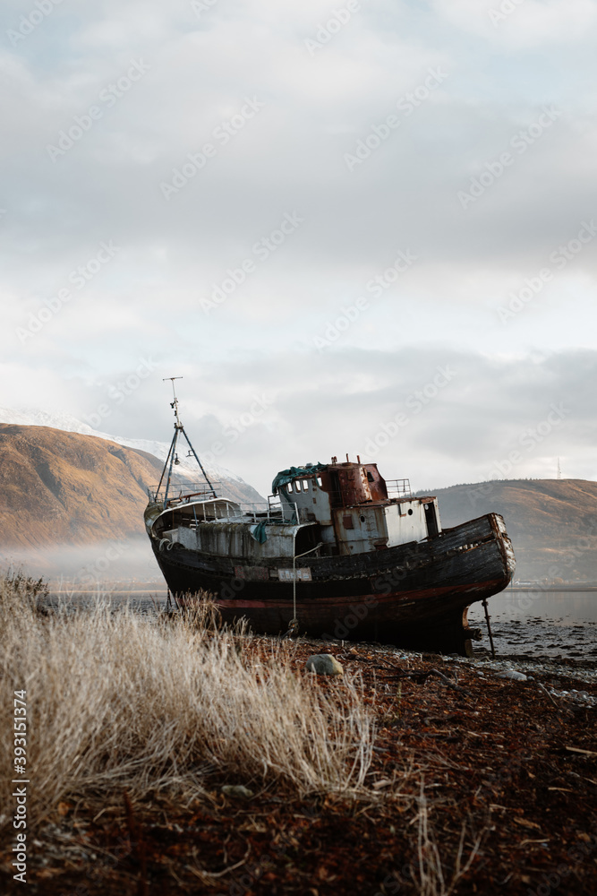 Old rusty fishing boat moored on beach in foggy morning in Scottish Highlands