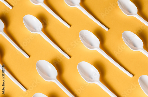 Top view flat lay composition of disposable white plastic spoons for takeaway food arranged on yellow background photo