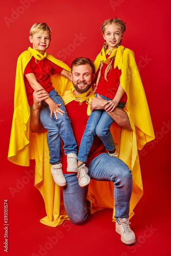 happy man holding super kids on shoulders posing at camera isolated over red background