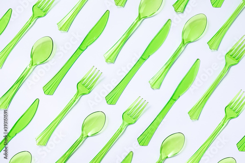 Top view composition of bright green transparent plastic cups with forks and spoons and knives placed on white background photo