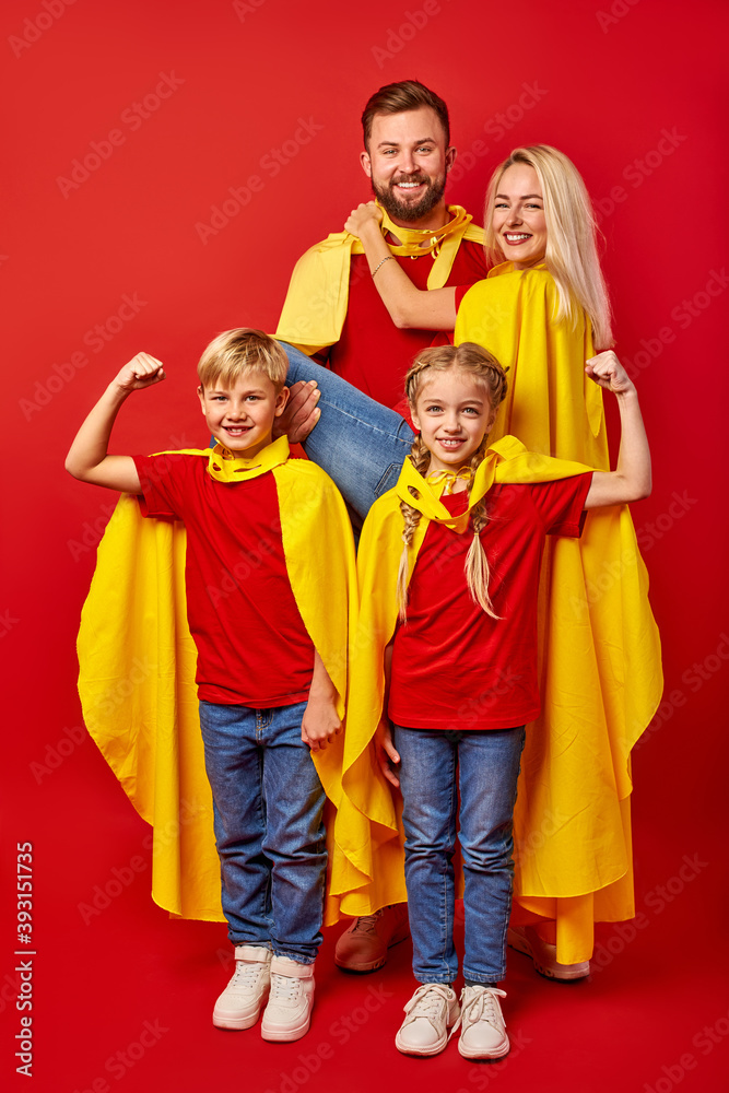 family pretending to be superhero in the park, beautiful happy parents and children in superhero costume posing isolated over red background. entertainment concept family pretending to be superhero in the park, beautiful happy parents and children in superhero costume posing isolated over red background. entertainment concept