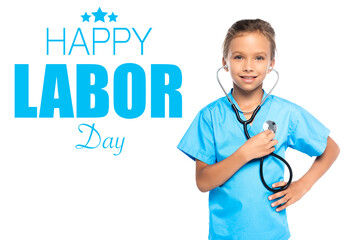 child in costume of doctor holding stethoscope while standing with hand on hip near happy labor day lettering on white