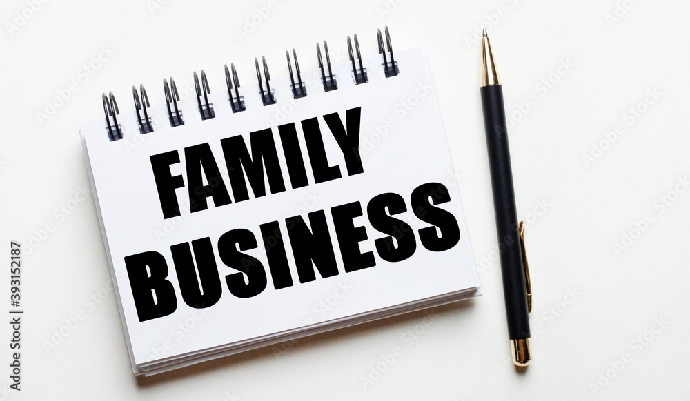 On a light background, a white notebook with the words FAMILY BUSINESS and a pen. On a light background, a white notebook with the words FAMILY BUSINESS and a pen.