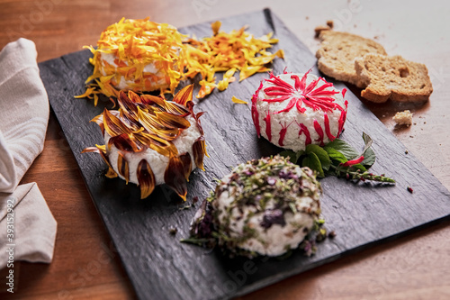 Delicious round shaped curd decorated with edible flower petals and placed on slate board on table in kitchen