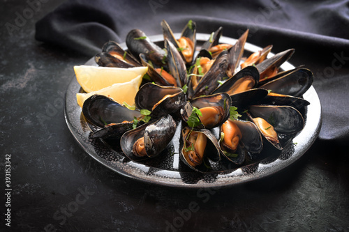 Mussels with lemon and parsley on a plate with a dark napkin on a black slate table, selected focus