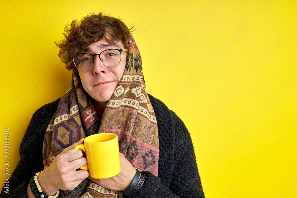 ill caucasian man isolated over yellow background, hold yellow cup with liquid medicine in it. male is drinking for better health, wearing warm clothes ill caucasian man isolated over yellow background, hold yellow cup with liquid medicine in it. male is drinking for better health, wearing warm clothes