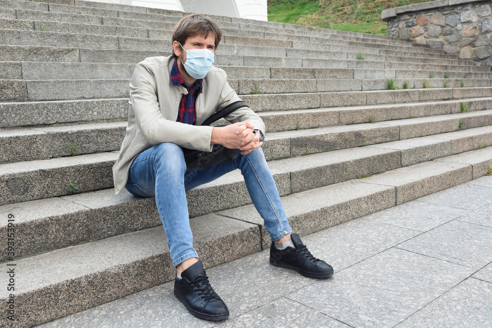 An office worker wearing a medical mask, fired from his job, sits on the steps of the street. Unemployment is rising due to the economic crisis. Depression, despair