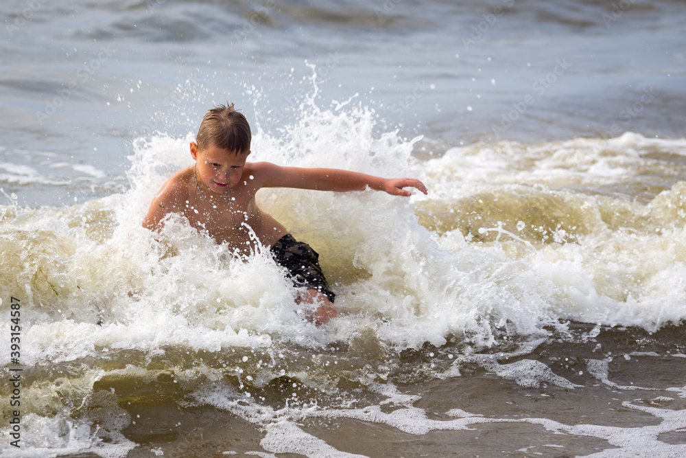 Young cheerful boy having fun at sea waves.