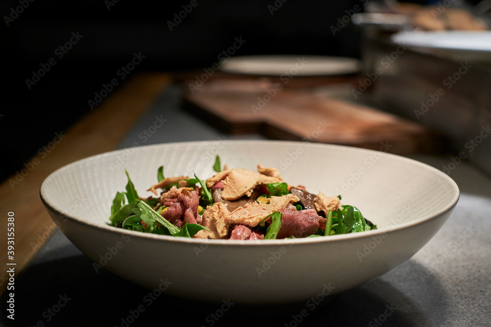 Bowl with delicious salad made with meat and fresh green rocket leaves placed on kitchen counter in restaurant Bowl with delicious salad made with meat and fresh green rocket leaves placed on kitchen counter in restaurant