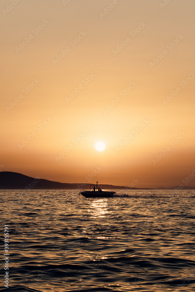 Silhouette of lonely marine vessel floating on rippling sea water against orange sunset sky in Croatia Silhouette of lonely marine vessel floating on rippling sea water against orange sunset sky in Croatia