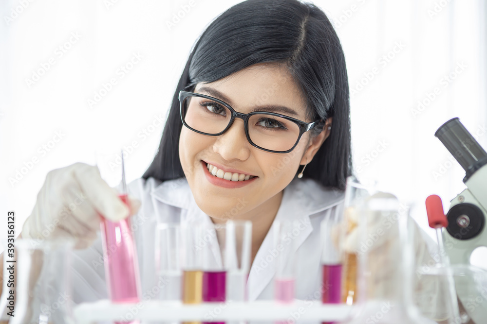 Young Asian scientist woman holding and looking at the chemical flasks in the laboratory